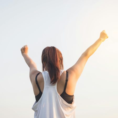 A woman celebrates success with arms raised in a bright outdoor setting.